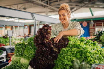 Smiling female greengrocer selling lettuce at agronomy fair.