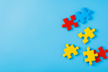 Fototapeta premium Blue, yellow, red pieces of puzzle on light blue background. World autism awareness day concept. Top view, copy space