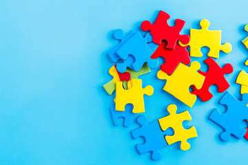 Obraz premium Blue, yellow, red pieces of puzzle on light blue background. World autism awareness day concept. Top view, copy space