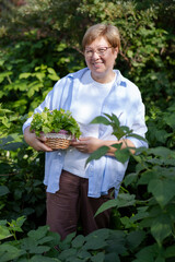 Senior woman stands with a basket of parsley in her garden