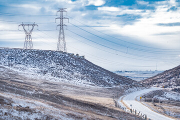 Electrical Pylons on a hilltop with power lines hanging over a valley overlooking winding road in Alberta Canada.