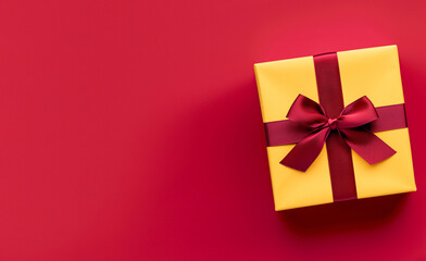 A yellow box with a red bow on top of a red background. The box is the center of attention and the red background emphasizes its color