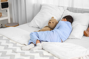 Cute little boy with teddy bear sleeping in bedroom