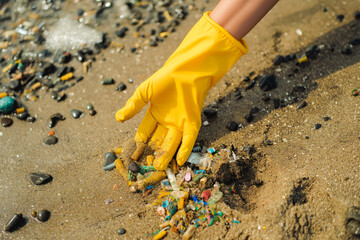 Volunteer hand with yellow gloves collect micro plastics collects plastic from beach sand. Environment, pollution, plastic waste concept