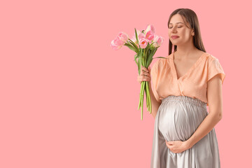 Young pregnant woman with tulips on pink background