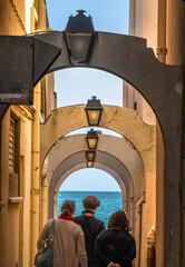 People walking through narrow street with arcades towards the sea