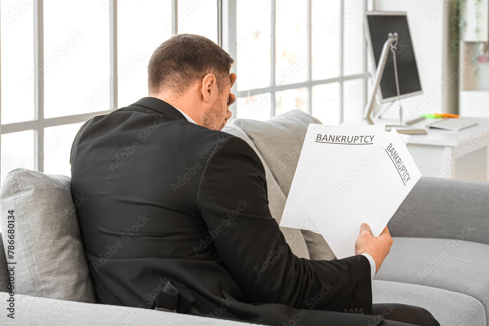 Wall mural Bankrupt businessman with papers sitting on sofa in office, back view