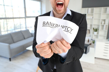 Angry businessman crumpling paper in office. Bankruptcy concept