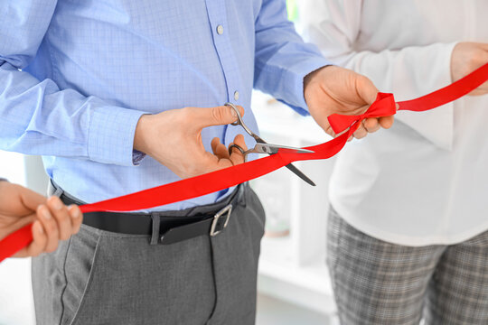 Business man cutting red ribbon in office, closeup
