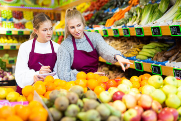 Focused woman grocery store owner giving instructions to young salesgirl, pointing at goods while...