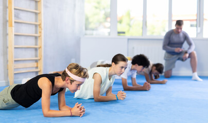 Group of preteen children doing push-ups on sports mats during a self-defense class in a gym