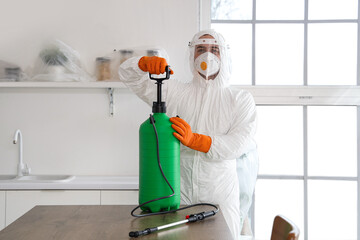 Male worker with disinfectant cylinder at table in kitchen