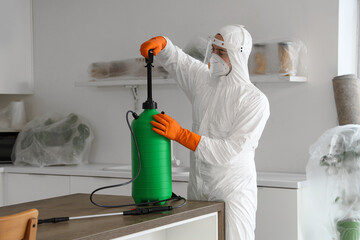 Male worker with disinfectant cylinder at table in kitchen