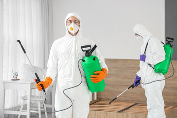 Male workers in hazmat suits disinfecting bedroom