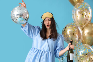 Drunk young woman with disco ball and champagne after Birthday party on blue background