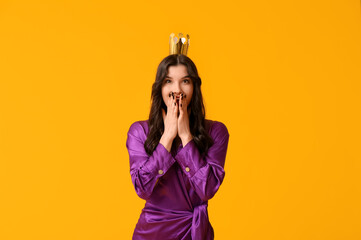 Surprised young woman in stylish prom dress and paper crown on yellow background