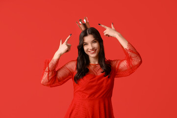 Beautiful young woman in stylish prom dress pointing at paper crown on red background © Pixel-Shot