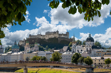 Salzburg, Austria, August 15, 2022. Stunning postcard of the historic center with the branches of a tree framing the fort on the hill, below the pedestrian bridge of love with glittering padlocks.