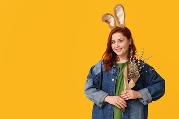 Beautiful young woman in bunny ears with pussy willow branches on yellow background. Easter...