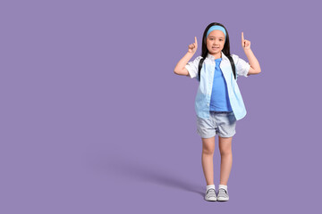 Portrait of fashionable little girl pointing up on lilac background
