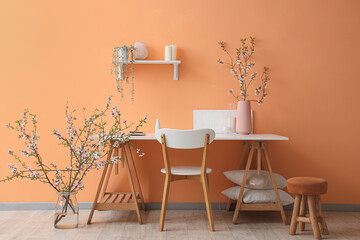 Cozy workspace decorated with blooming branches near orange wall