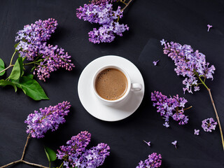 top view a cup of coffee on a black table and blooming lilac branches
