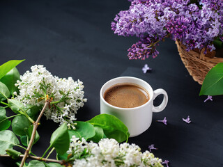 cup of espresso coffee on the table with branches of blooming white and purple lilacs. Spring time