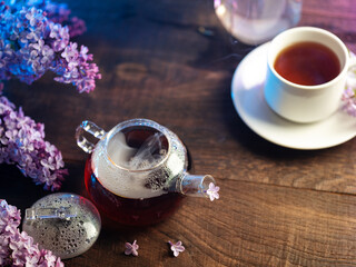 A cup of lilac tea and a teapot on a wooden table. Branches of blooming lilac . Hot spring healthy tea
