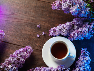 A tea cup on a wooden table and a bouquet of blooming lilacs. Copy space