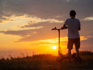 young man on an electric scooter in a field at sunset. Stand and admire the beautiful sunset