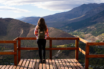 Fototapeta na wymiar Unrecognizable young woman in sportswear observing the scenery from a wooden tourist lookout overlooking the mountains of Patagonia Argentina. Space for text.