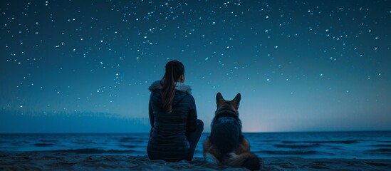 Woman and german shepherd admiring starry night sky by sea coast, sitting together, rear view