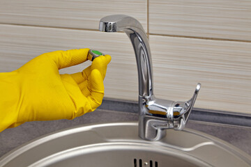 A hand in yellow gloves holds a faucet aerator to replace it