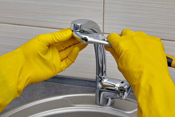 Repairman in yellow gloves with an adjustable wrench changes the faucet aerator
