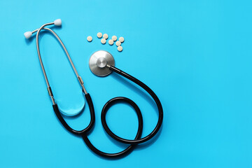 Stethoscope and white pills on a blue background, top view. Cardiology and healthcare concept....
