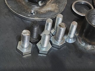 Close-up view of a diverse selection of bolts, nuts, and screws arranged neatly on a dark textured...