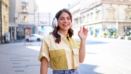 Happy young Mexican woman with headphones enjoying music on the street