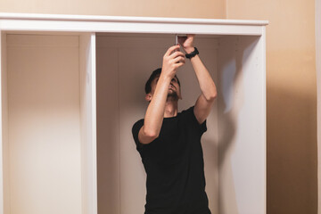 A young man is tightening the screws inside in the wardrobe.