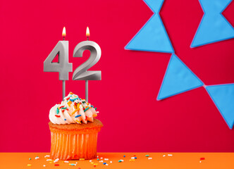 Number 42 candle with birthday cupcake on a red background with blue pennants