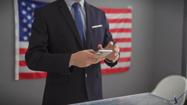 Professional hispanic man in a suit using a smartphone with american flag in background, indoors.