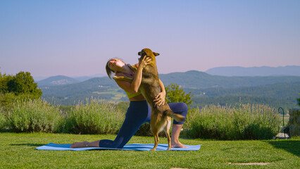 Lively dog jumps and hugs a lady practicing crescent lunge yoga pose in garden