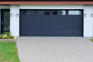 A modern black metal exterior garage door with four small horizontal glass windows. The modern door...