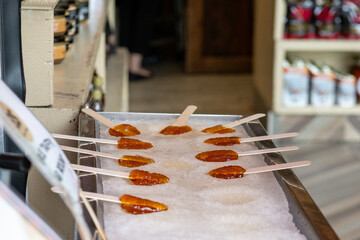A traditional Canadian sweet candy made of boiled maple sap laid on a tray of clean snow. A male rolls thick syrup into a round lollipops using a small wooden stick. A street vendor sells the pops.
