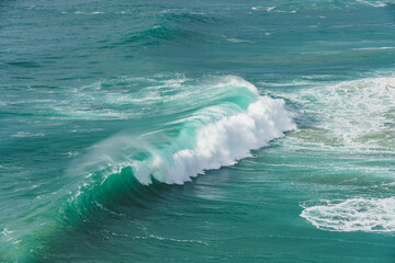 A magnificent wave curls with frothy white foam at Nazare, known for its big wave surfing. - 786721151