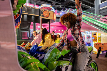 African American teenage girl celebrates victory in the arcade motorcycle race with her multiethnic...