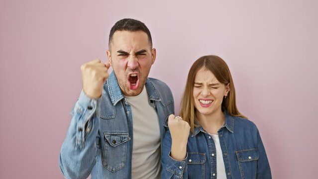 Beautiful couple, standing fuming over a pink wall, wearing denim shirts. spill of anger, fists clenched in furious, frustrated rage. perfect crazy love gone mad.
