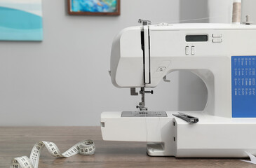 White sewing machine and measuring tape on wooden table indoors