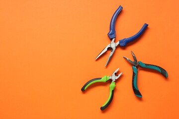 Different pliers on orange background, flat lay. Space for text