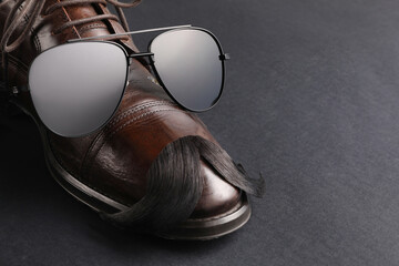 Artificial moustache, shoe and sunglasses on black background, closeup. Space for text