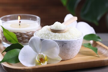 Obraz na płótnie Canvas Natural sea salt in bowl, candle and beautiful orchid flower on wooden table, closeup